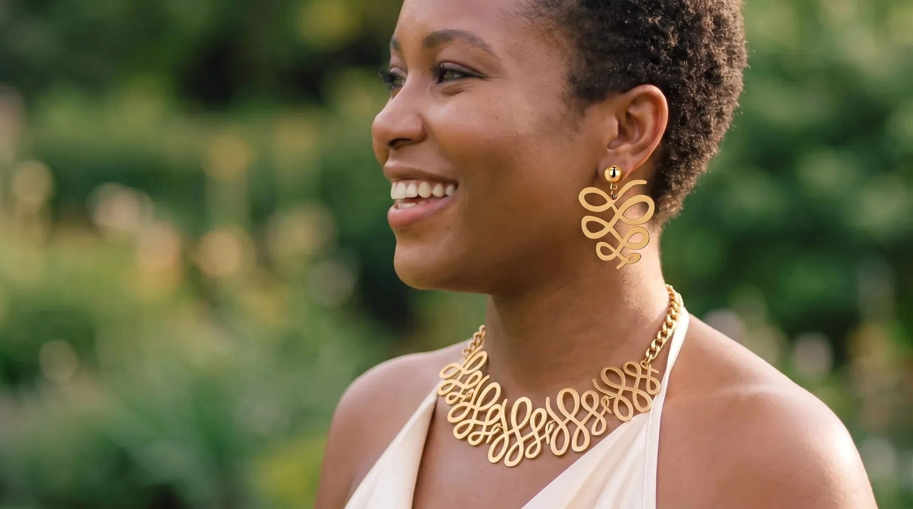 A woman in a cream satin top wearing the Ripple Set: a gold swirl collar and matching swirl earring