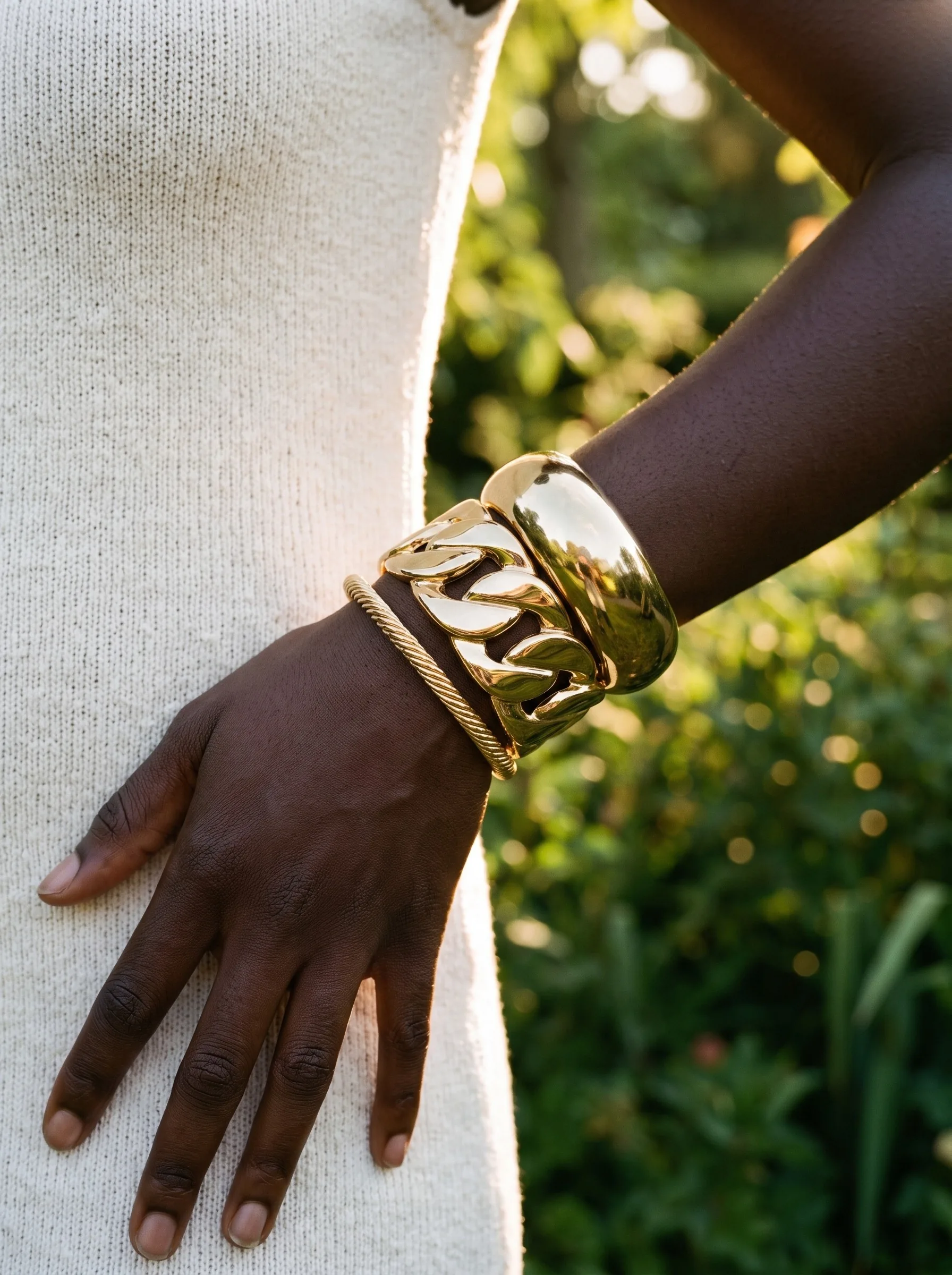 A wrist with a gold dome cuff, a chain-link cuff and a rope bangle